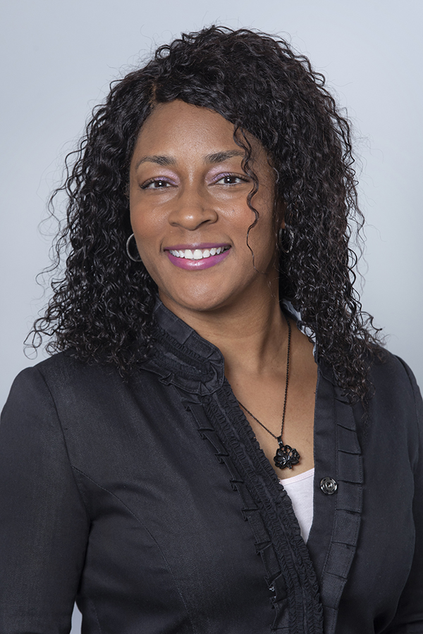 tara-mcknight-virtuerenity Smiling woman with curly hair wearing a black top and necklace.